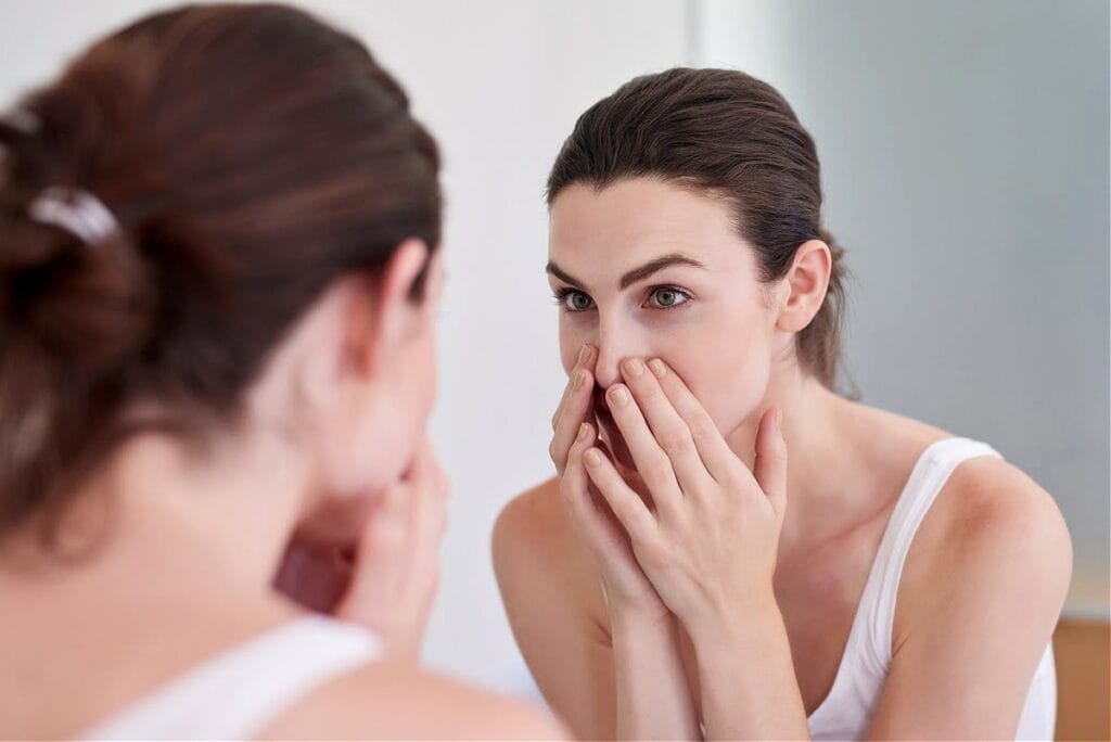 Woman touching skin in bathroom mirror