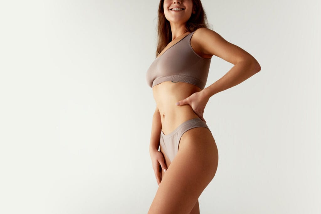 Cropped portrait of woman in sports bra and underwear set, confidently placing hands on her hips against studio background